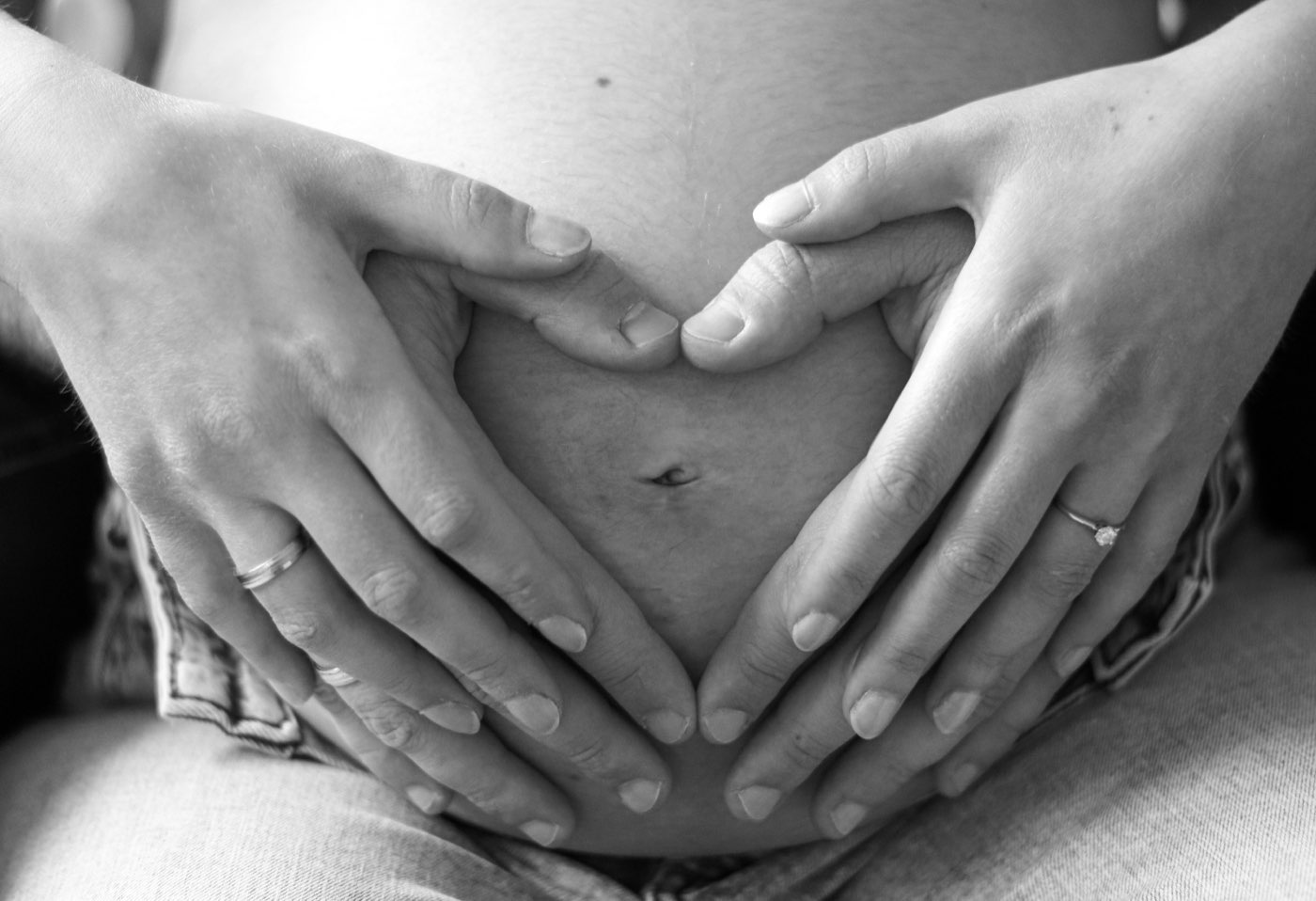 Schwarzweißaufnahme: Zwei Hände formen ein Herz auf dem Babybauch