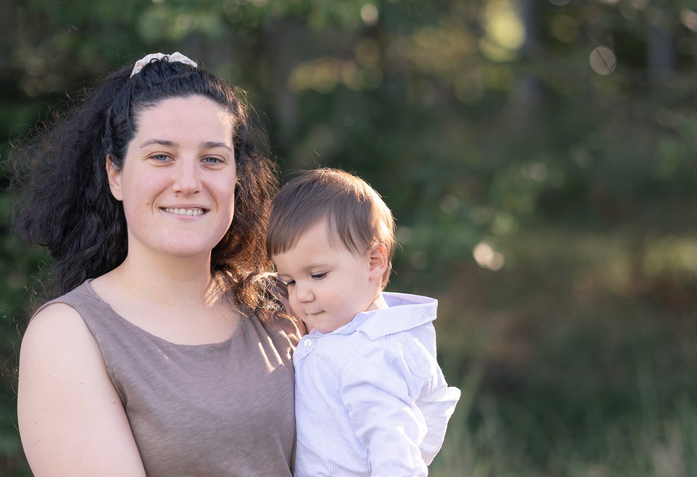 Eine Mama l&auml;chelt, ihr Kleinkind lehnt sich an sie