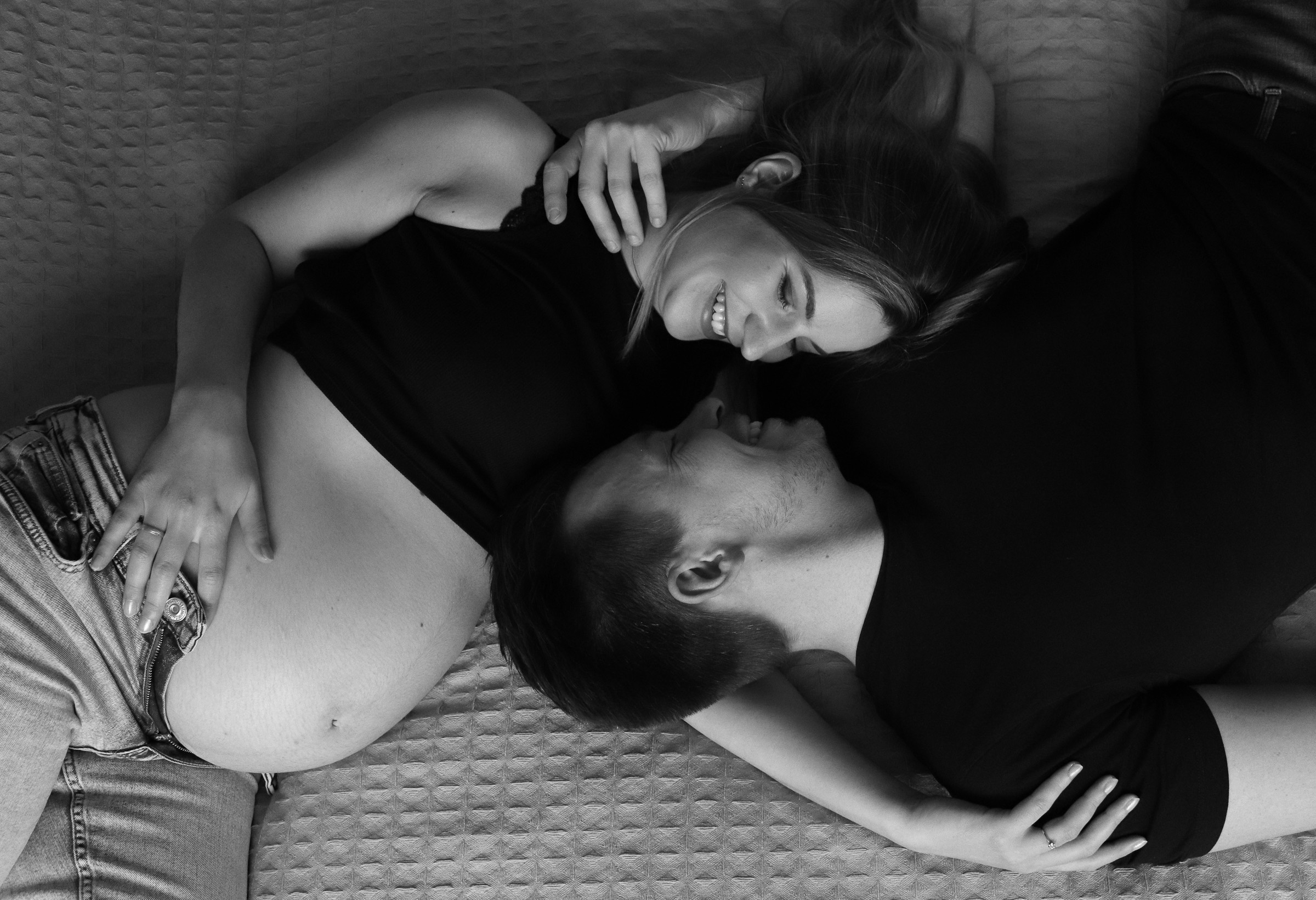 Ein Paar liegt nebeneinander, seine Wange am Babybauch