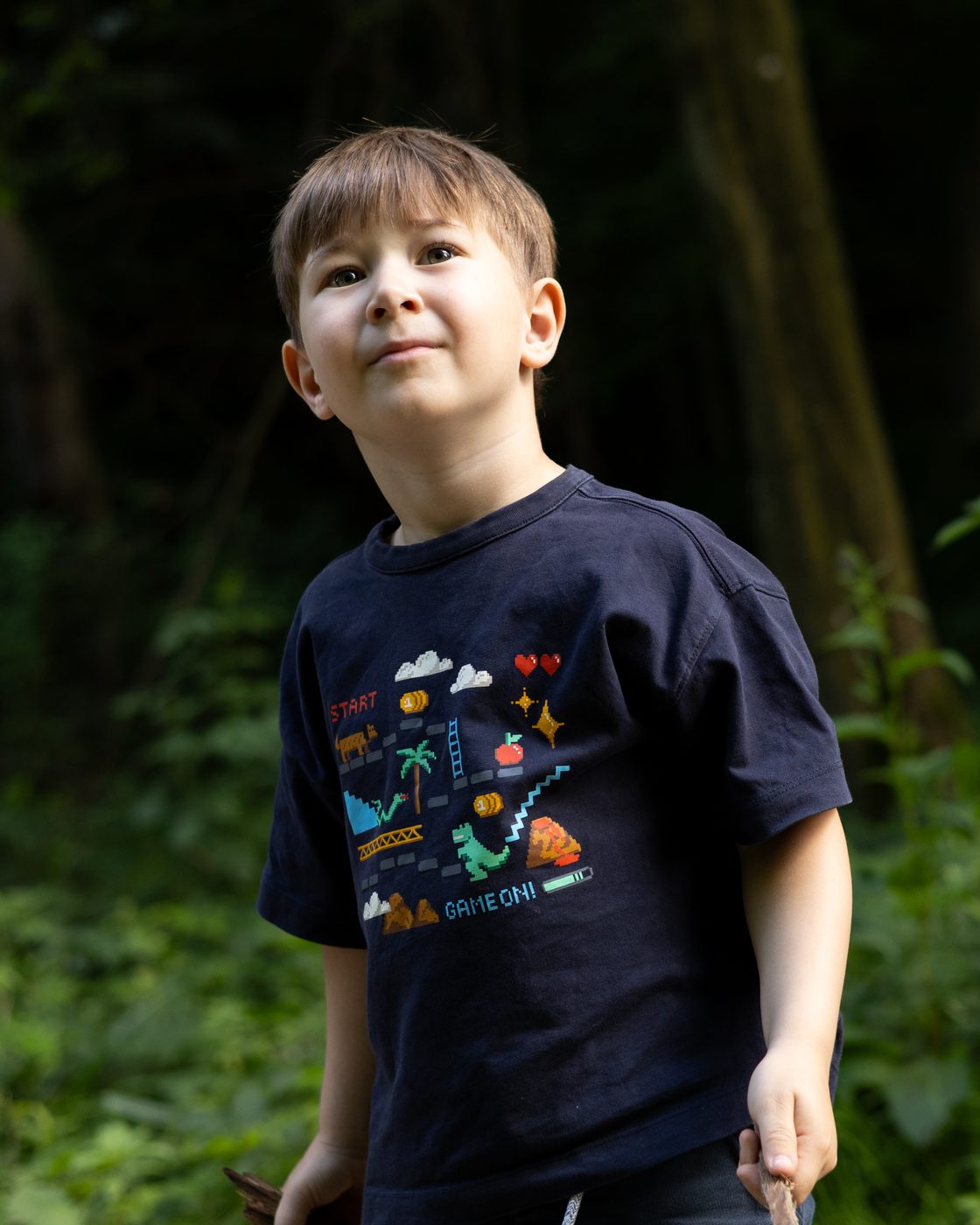 Ein Bub im dunklen T-Shirt steht im Wald und schaut nach oben
