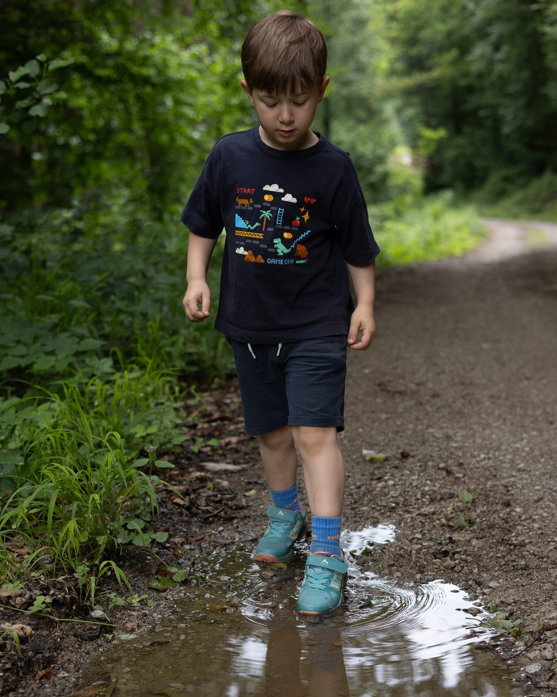 Der Bub stapft durch eine Pf&uuml;tze auf dem Waldweg