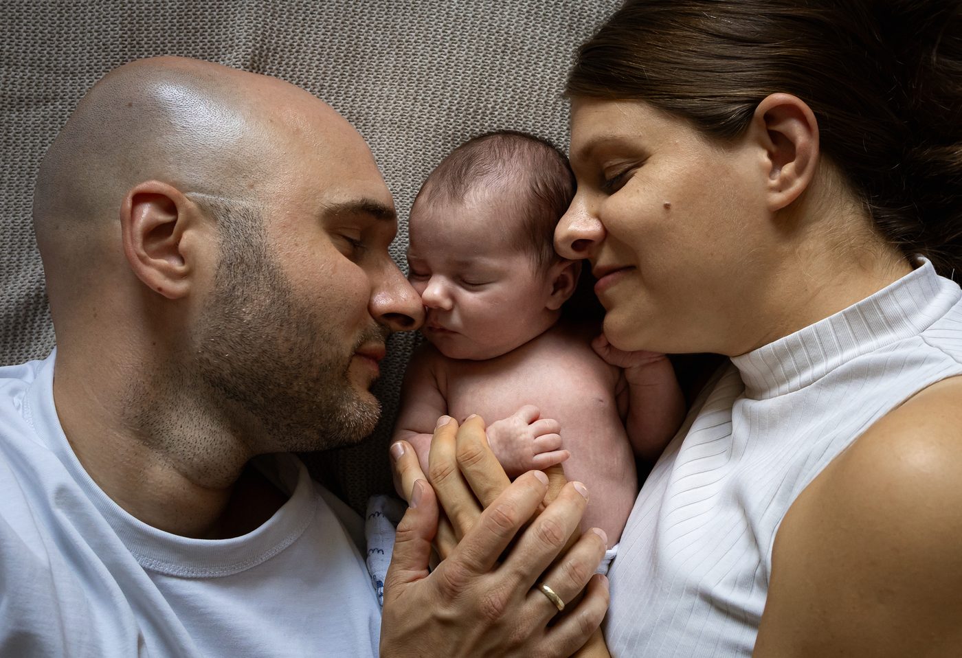 Mama und Papa kuscheln sich an ihr Neugeborenes, Wange an Wange
