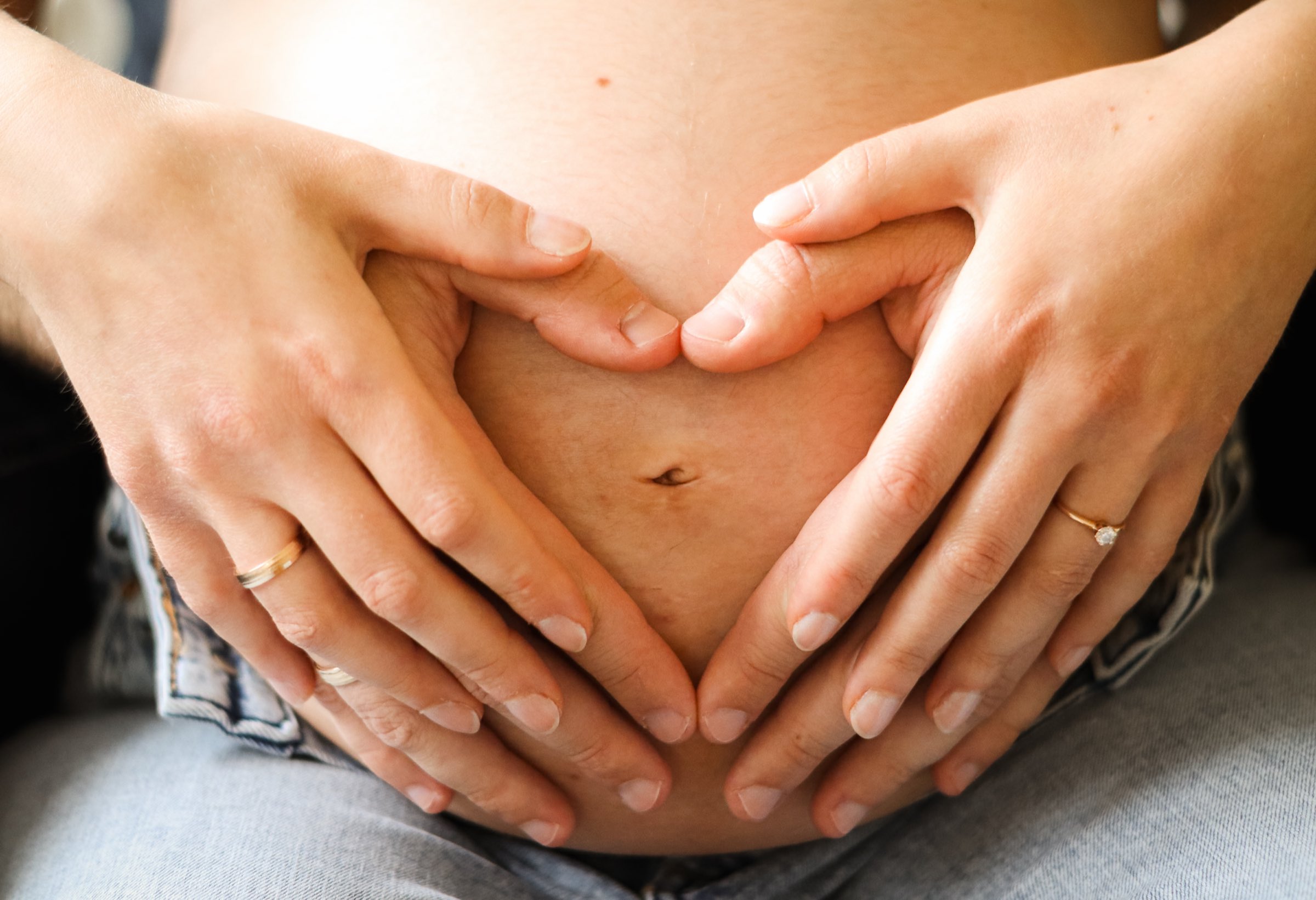 Vier H&auml;nde formen ein Herz auf einem Babybauch