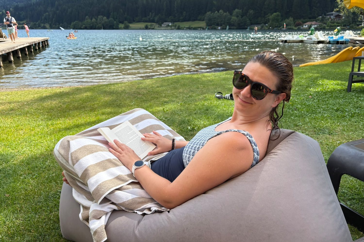 Kerstin liegt mit einem Buch auf einem Sitzsack am Seeufer und l&auml;chelt in die Kamera